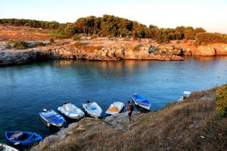 Delle barche legate sugli scogli di Porto Badisco al tramonto