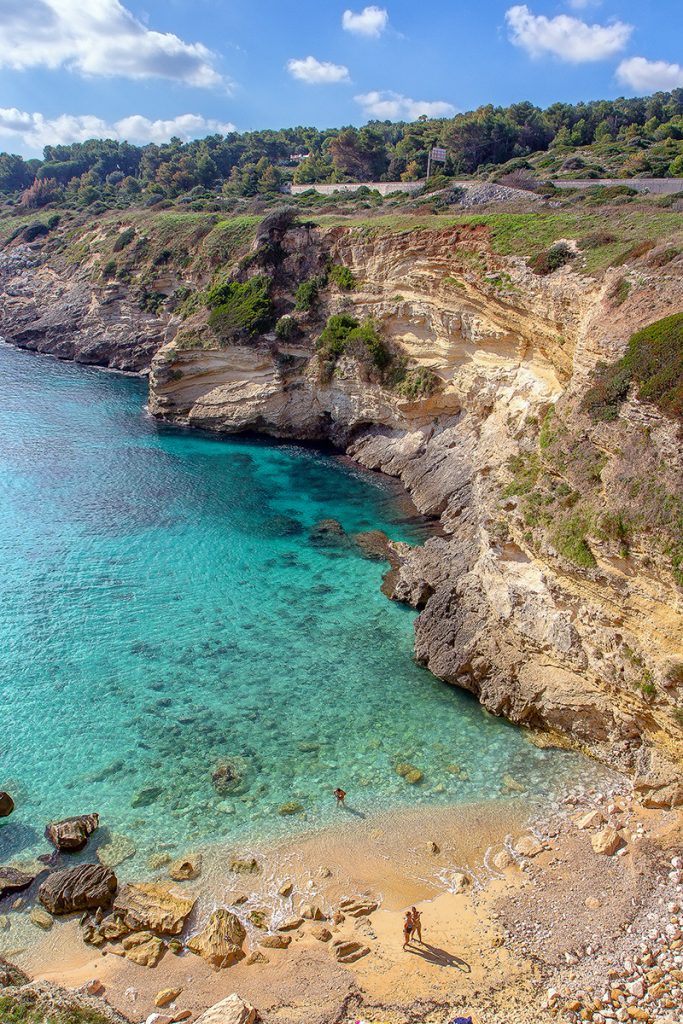 vista della baia di Porto Miggiano dall'alto con tre persone che fanno il bagno nell'acqua cristallina