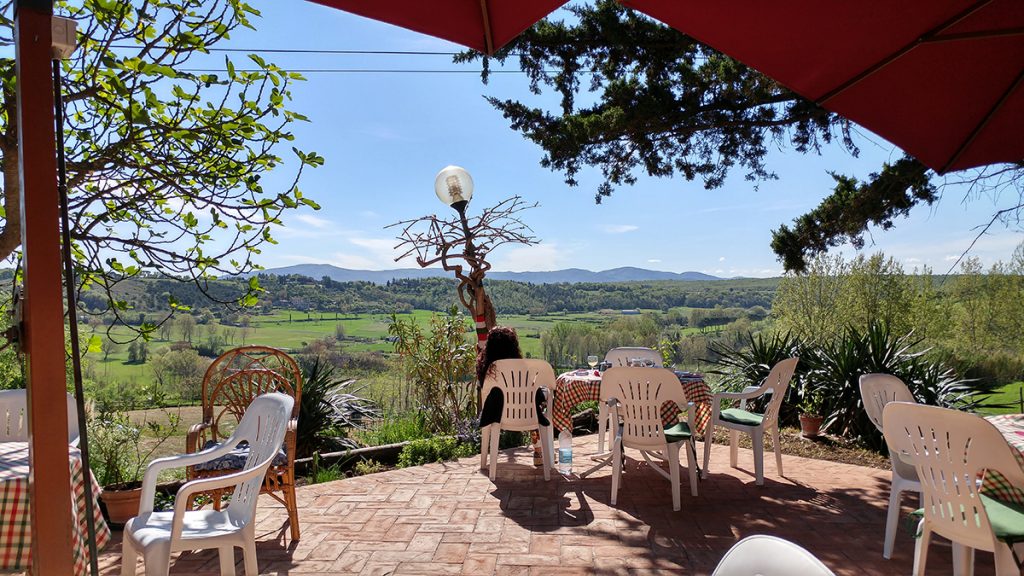 Scorcio della vista sulla Val D'elsa, con dei tavolini e una ragazza che prende il sole. Meta ideale su cosa vedere a San Gimignano